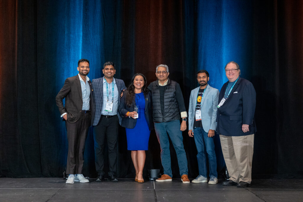 Clarisa James proudly accepts the Tech Pitch Competition Award on behalf of Kings III Emergency Communications at the 2024 AAHOA Convention & Trade Show, standing alongside last year’s esteemed panel of judges.
